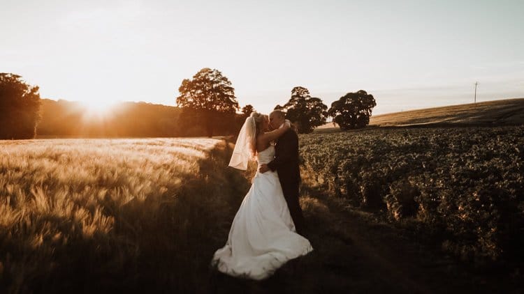 Bride and groom embracing in a field at sunset