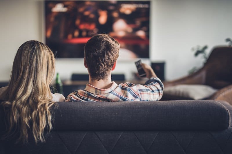 A couple on a sofa watching their wedding film on TV