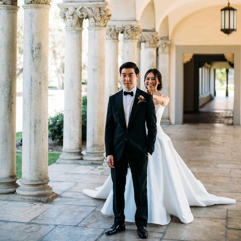 A bride walking up behind her groom for their first look in a colonnade