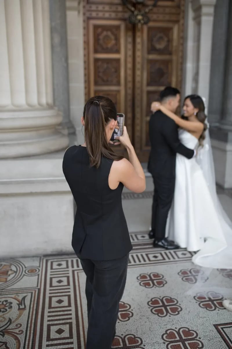 A wedding content creator filming a bride and groom on a phone in a grand doorway