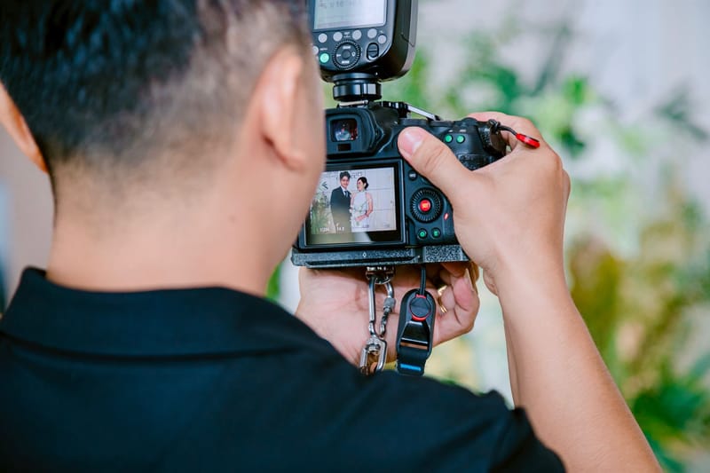 A wedding photographer with a flash on the camera reviewing a portrait of the couple on the screen