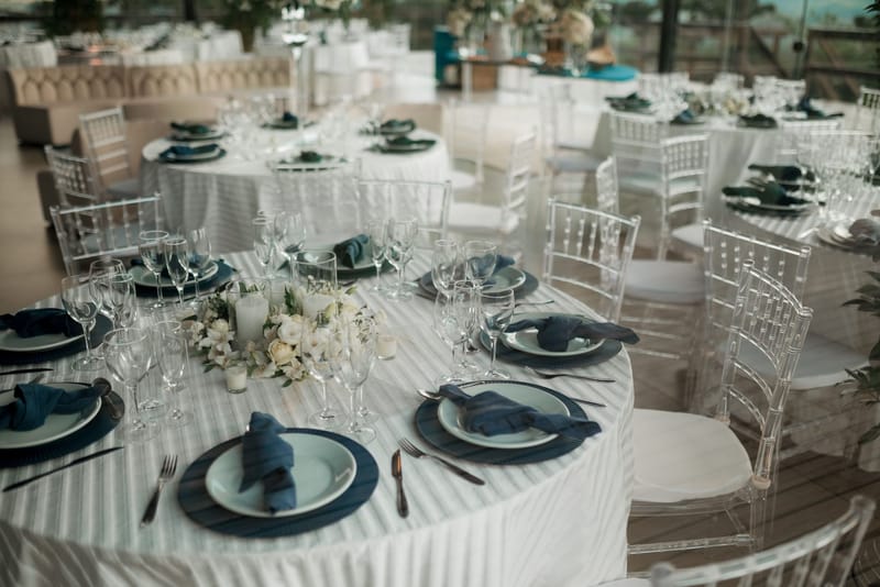 Round tables set for a wedding reception, with white flowers, candles and navy napkins