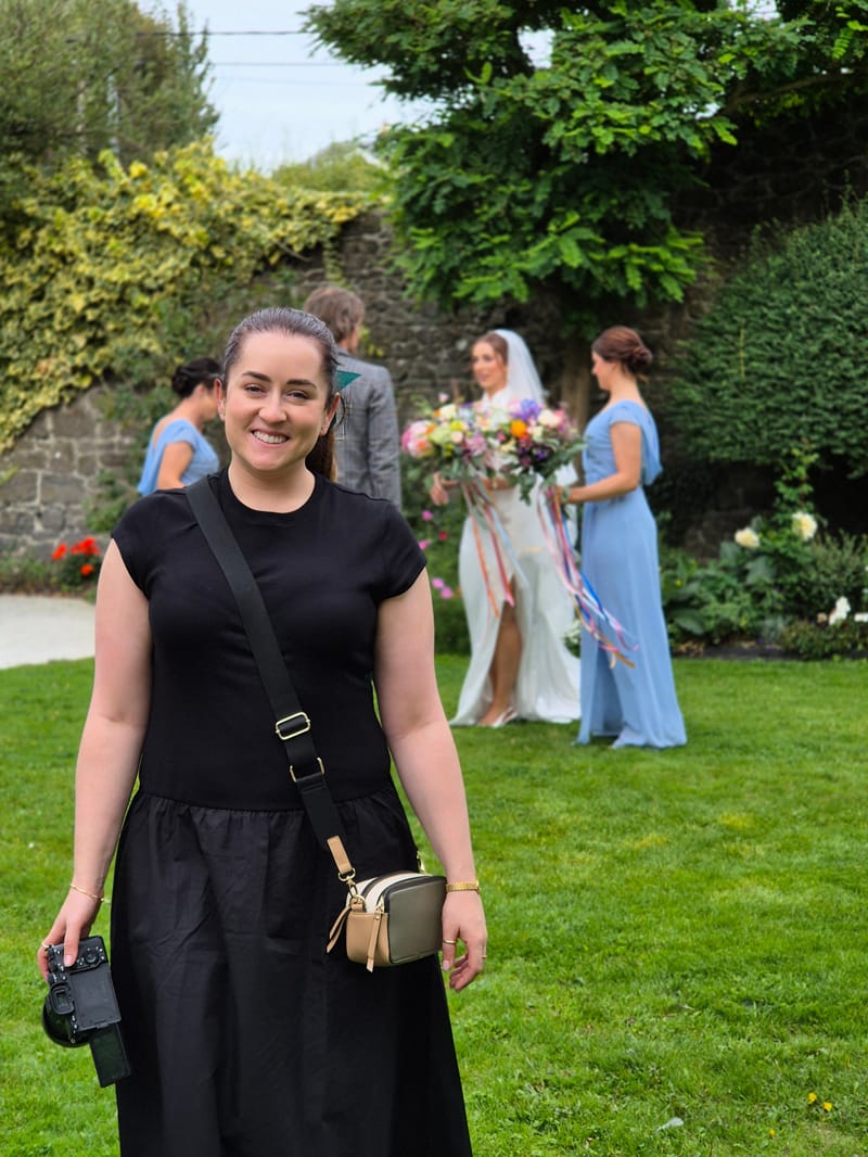 A wedding videographer at an outdoor Irish wedding, with the bride and bridesmaids behind her